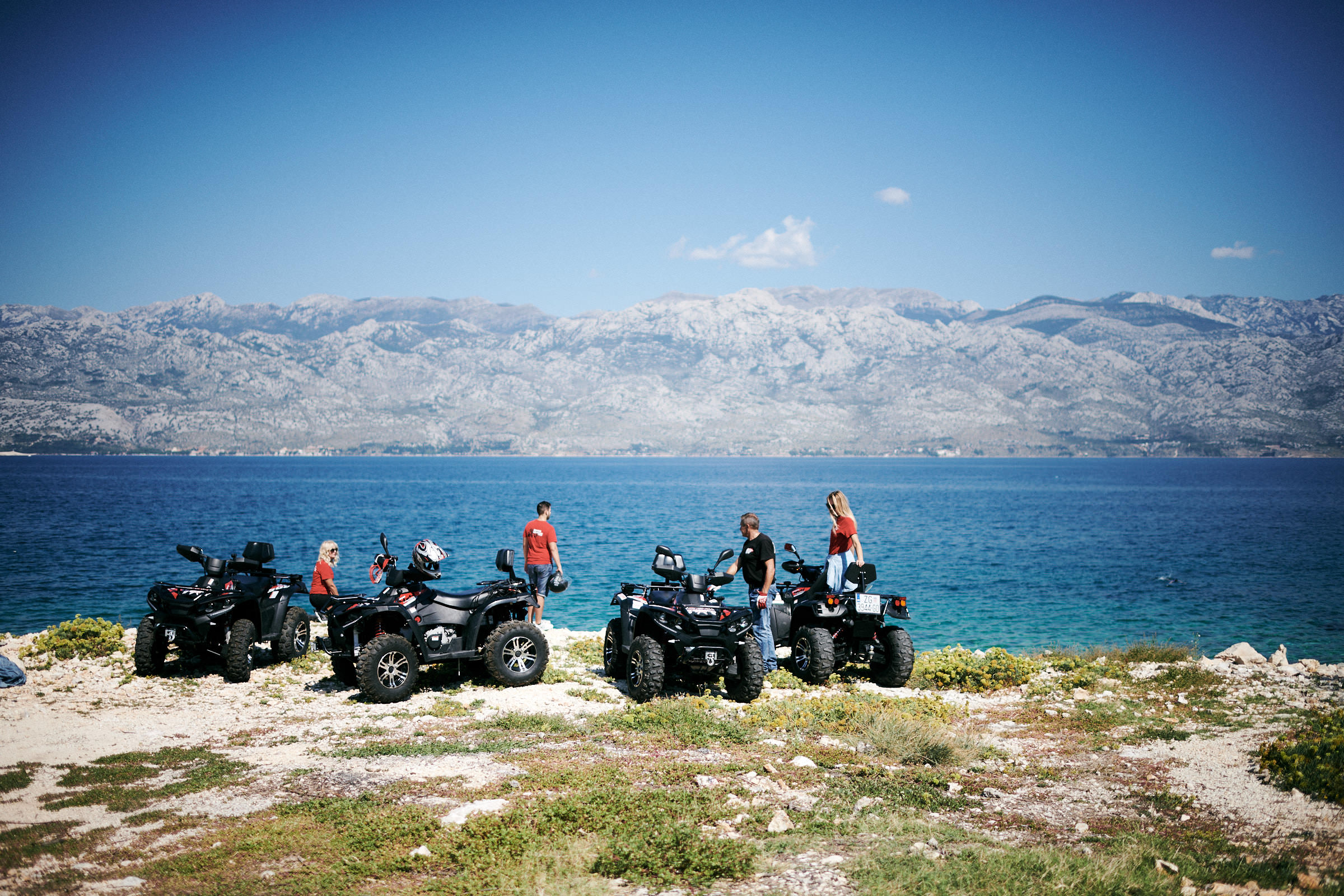 A quad-bike group stopped at a coastal viewpoint with the Velebit mountains across the channel