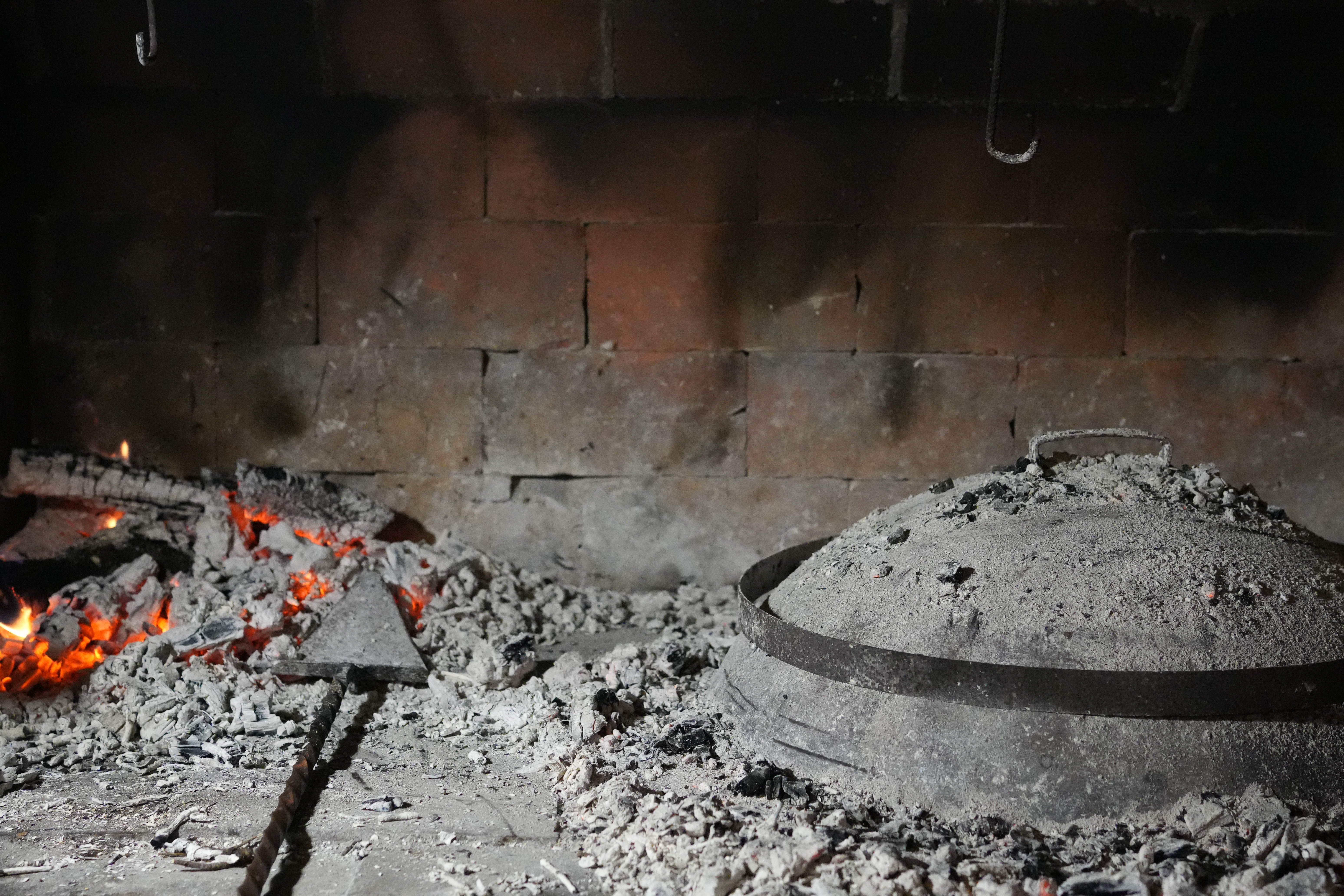 Croatian peka cooking under hot embers in a stone hearth