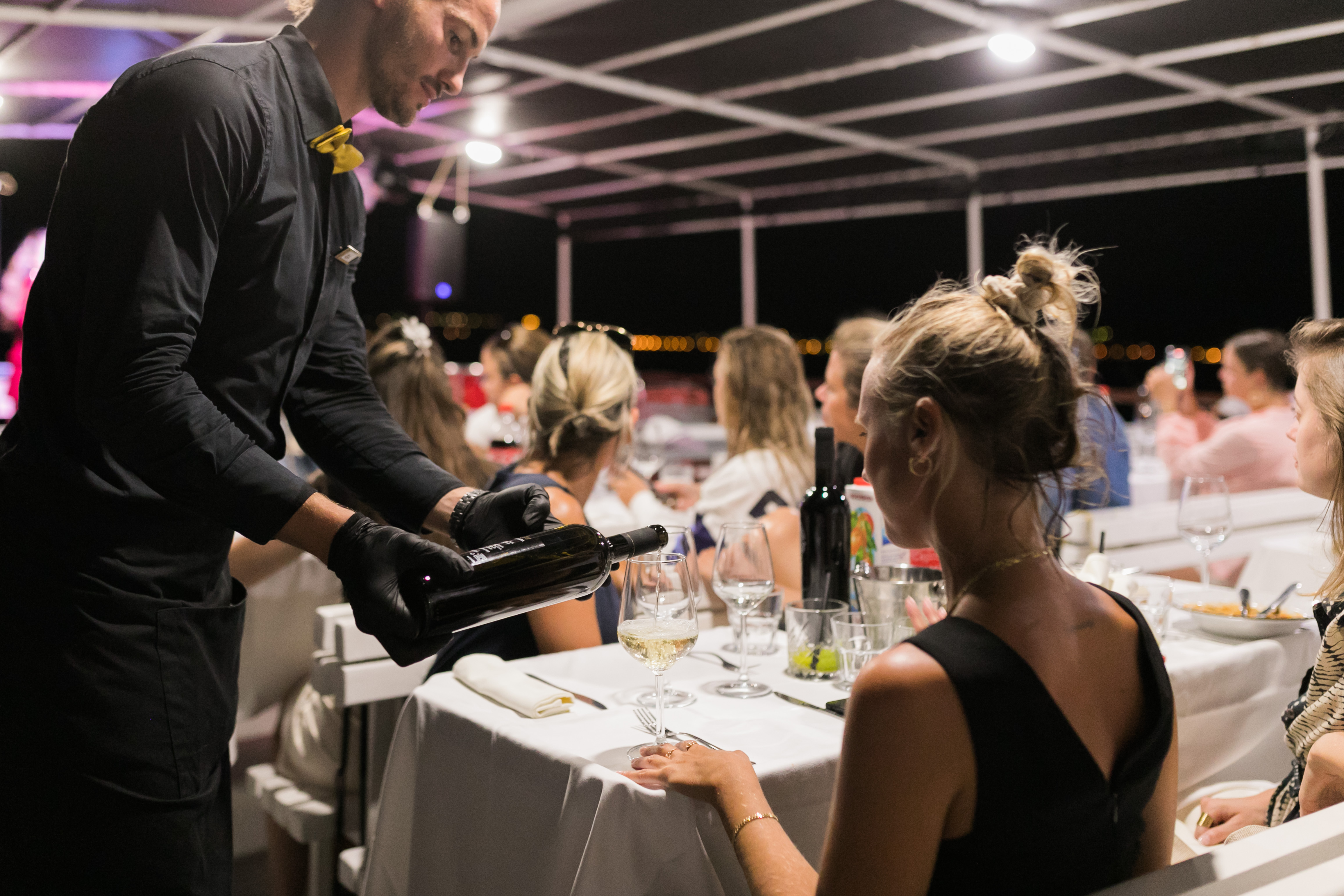 A sommelier pouring wine for guests at an evening dinner on a boat